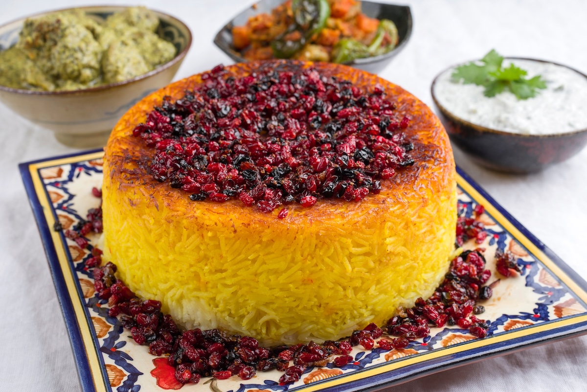 Arroz persa tahdig en un plato estampado, decorado con frutos secos, detrás cuencos con pequeños aperitivos.