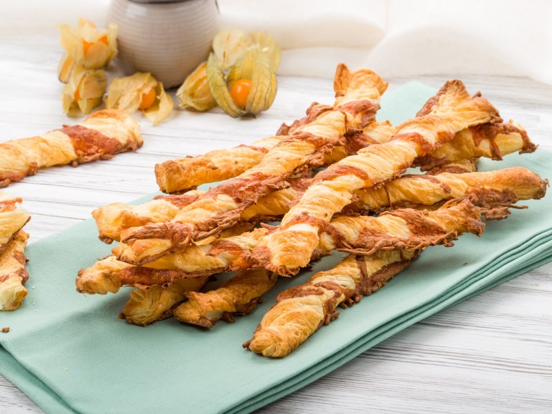 Varios palitos de queso hojaldrados sobre una servilleta azul.