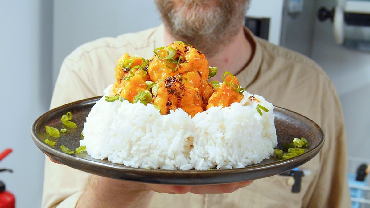 Un plato con una porción grande de arroz, sobre el cual se distribuyen los camarones Bang Bang. El chef Oli sostiene el plato hacia la cámara.