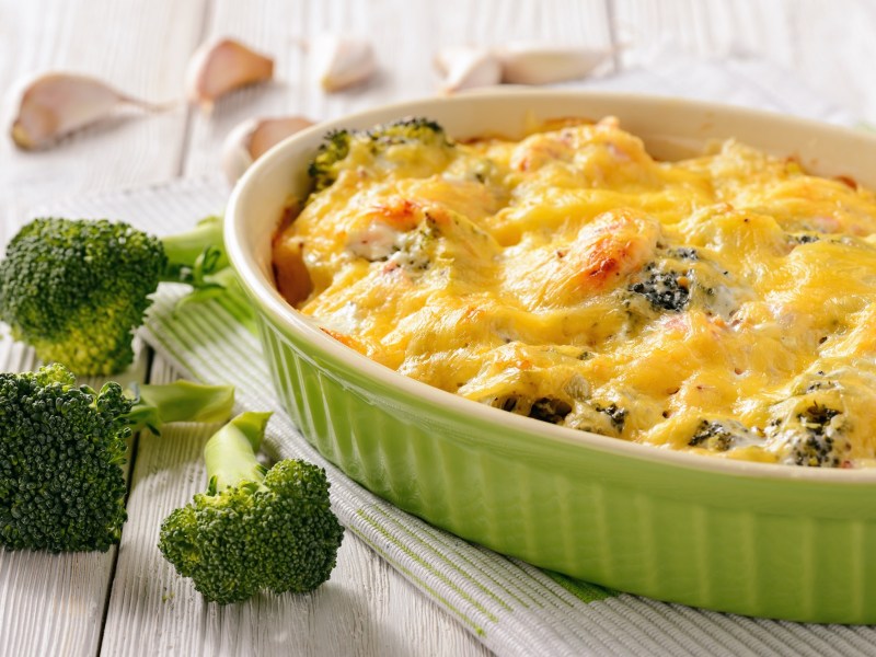 Una fuente para horno con pastel de brócoli y papa, junto a ramitos de brócoli y dientes de ajo.