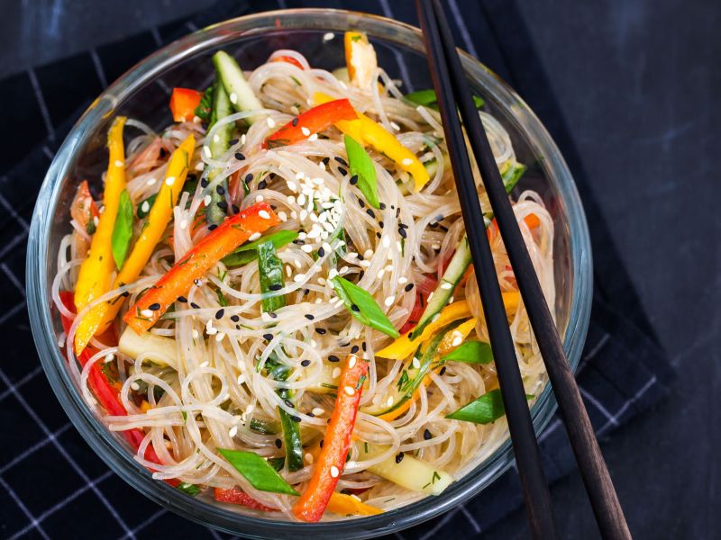 Ensalada de fideos de vidrio, servida en un tazón oscuro con palillos.