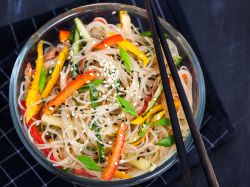 Ensalada de fideos de vidrio, servida en un tazón oscuro con palillos.