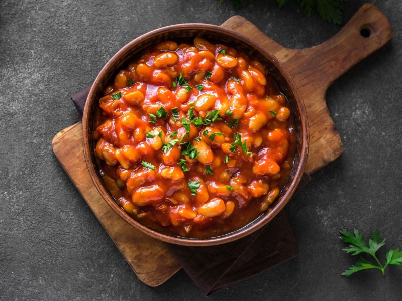 Frijoles al horno, servidos en una sartén de hierro fundido. Hierbas frescas como decoración. La sartén está sobre una tabla de madera.