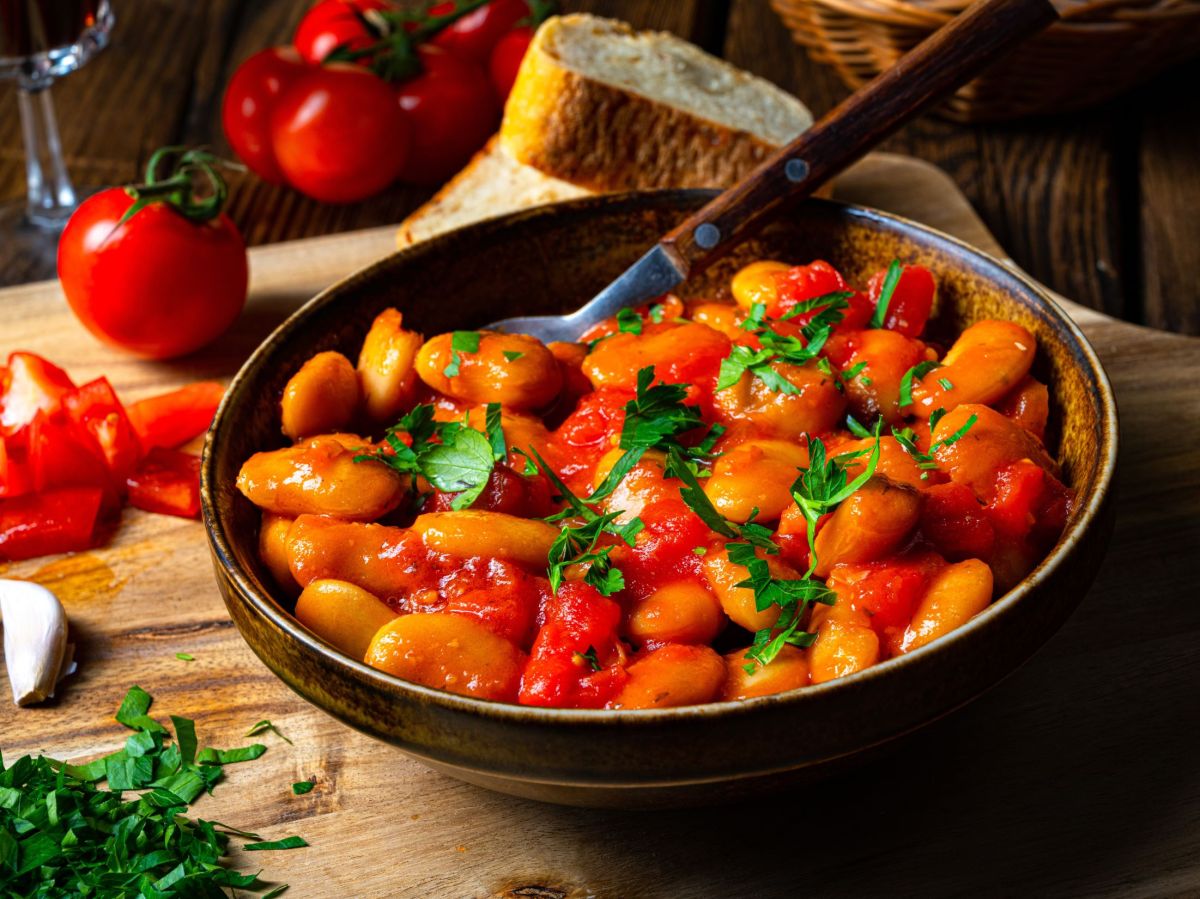 Frijoles blancos a la sartén, servidos en una sartén. Tomates y otras hierbas se encuentran a un lado como decoración.