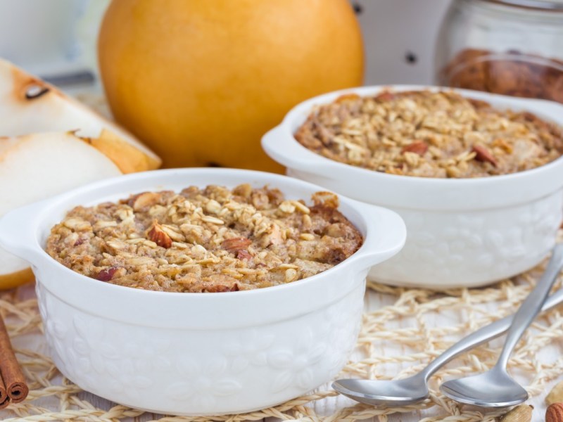 Dos pequeños moldes con gachas de avena al horno. Al fondo hay peras frescas.