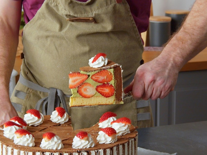 Se ve como un cocinero saca una porción de pastel de bizcochos de chocolate. En el fondo se ve un juego de cocina.