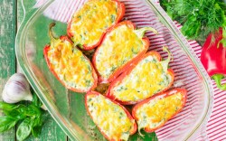 Pimientos rellenos de queso feta y arroz en una fuente transparente para horno vistos desde arriba.