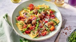 Un plato de ravioles al horno con verduras, albóndigas y rúcula.