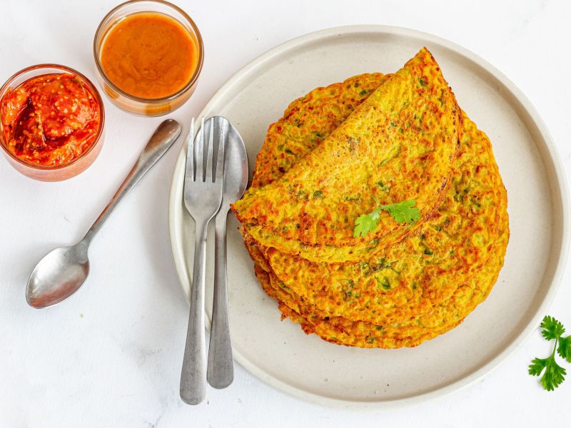 Tortitas de lentejas, servidas en un plato blanco. Junto a ellas hay cubiertos, una cuchara pequeña y dos tazones con salsas.