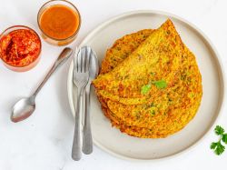 Tortitas de lentejas, servidas en un plato blanco. Junto a ellas hay cubiertos, una cuchara pequeña y dos tazones con salsas.